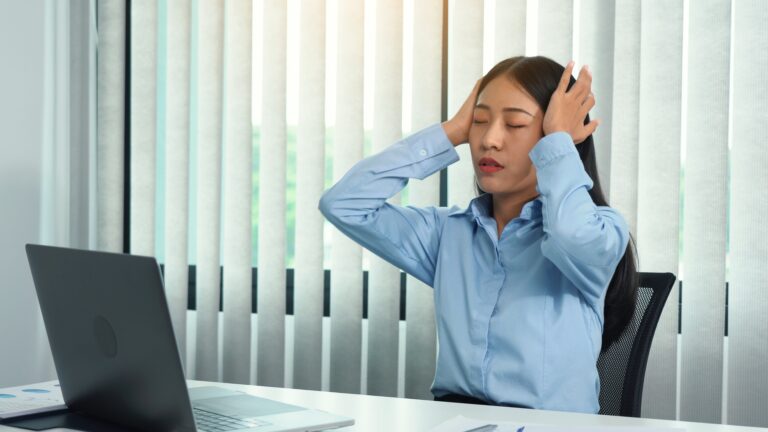 Asian woman sitting at work caused a headache so she gently rubbed her head with her hand.