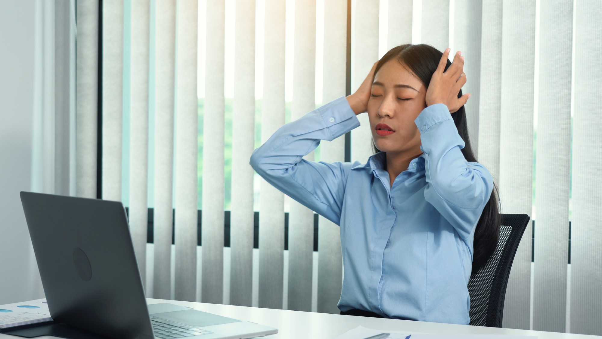 Asian woman sitting at work caused a headache so she gently rubbed her head with her hand.