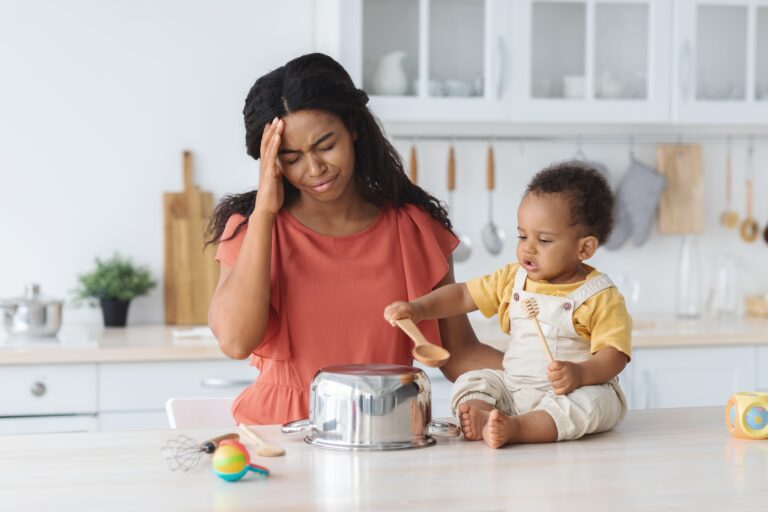 Black mother suffering headache while her infant baby making noise in kitchen